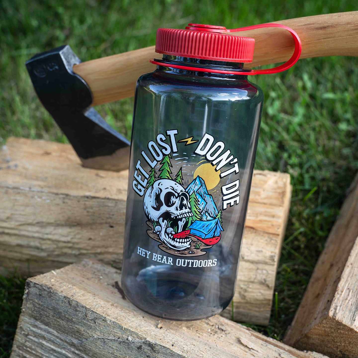 Clear water bottle with red lid featuring a skull graphic and text, placed on wooden logs with an axe in the background.